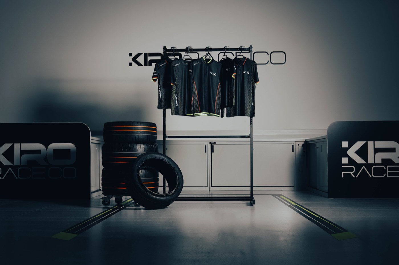 Rail of black team shirts in a studio set with racing tyres and the team backdrop behind