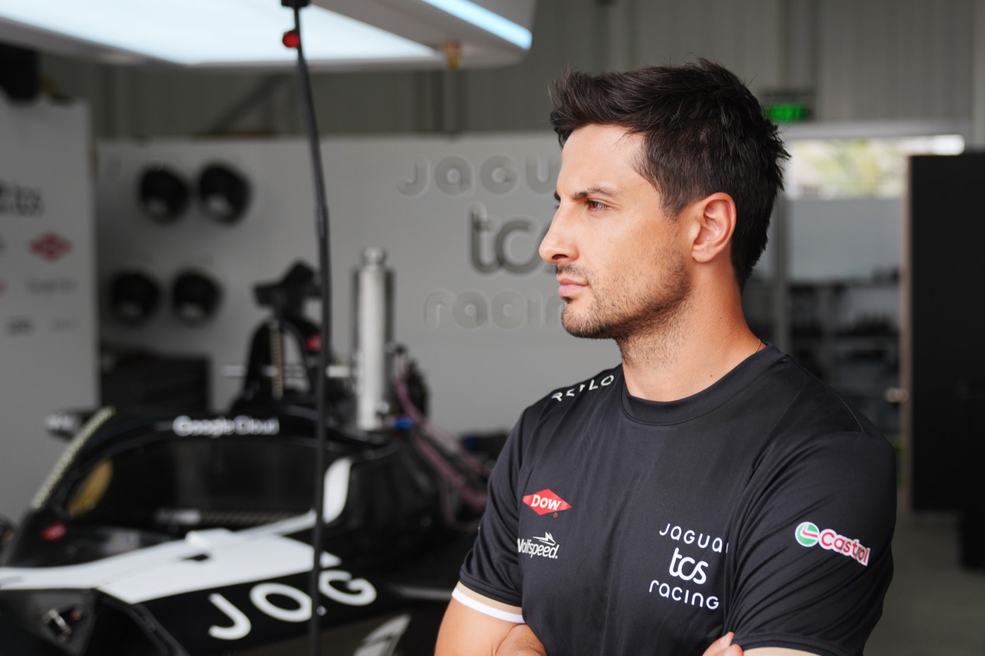 Team member in a black Reflo team polo standing arms folded in the race garage beside the car